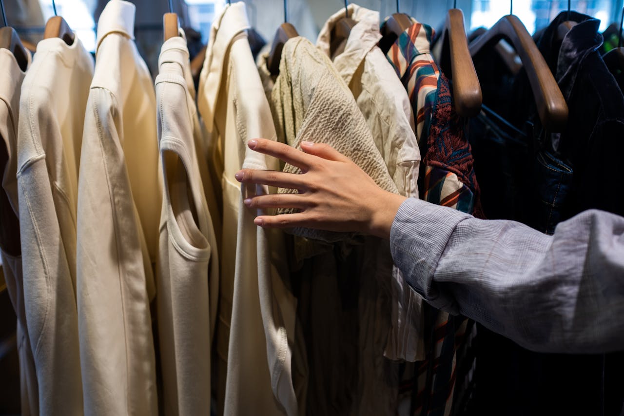 services-03 A shoppers hand browsing clothes in a retail store, focusing on fabric textures.
