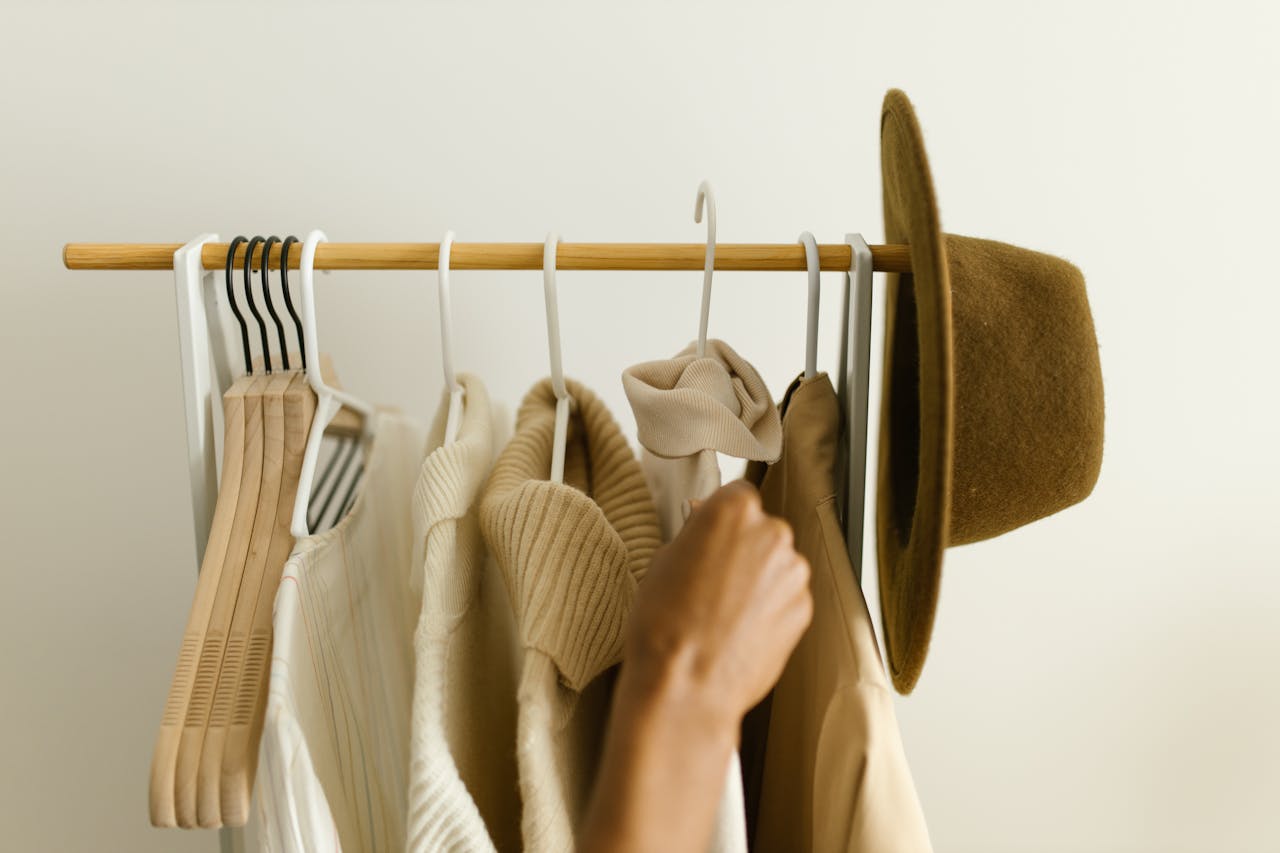 about-us Stylish beige and brown clothes on a rack with a hand reaching in.