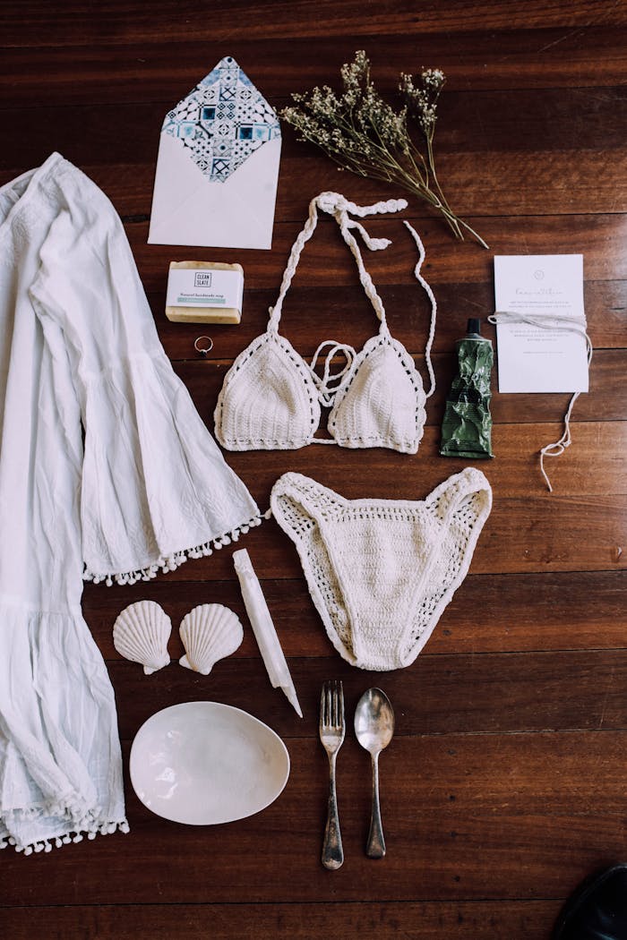 who-we-are Bohemian style flat lay with crochet bikini, dress, and travel essentials on wooden floor.
